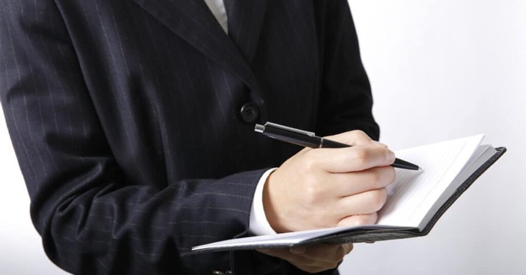 ノートを手にペンを握るスーツ姿の男性